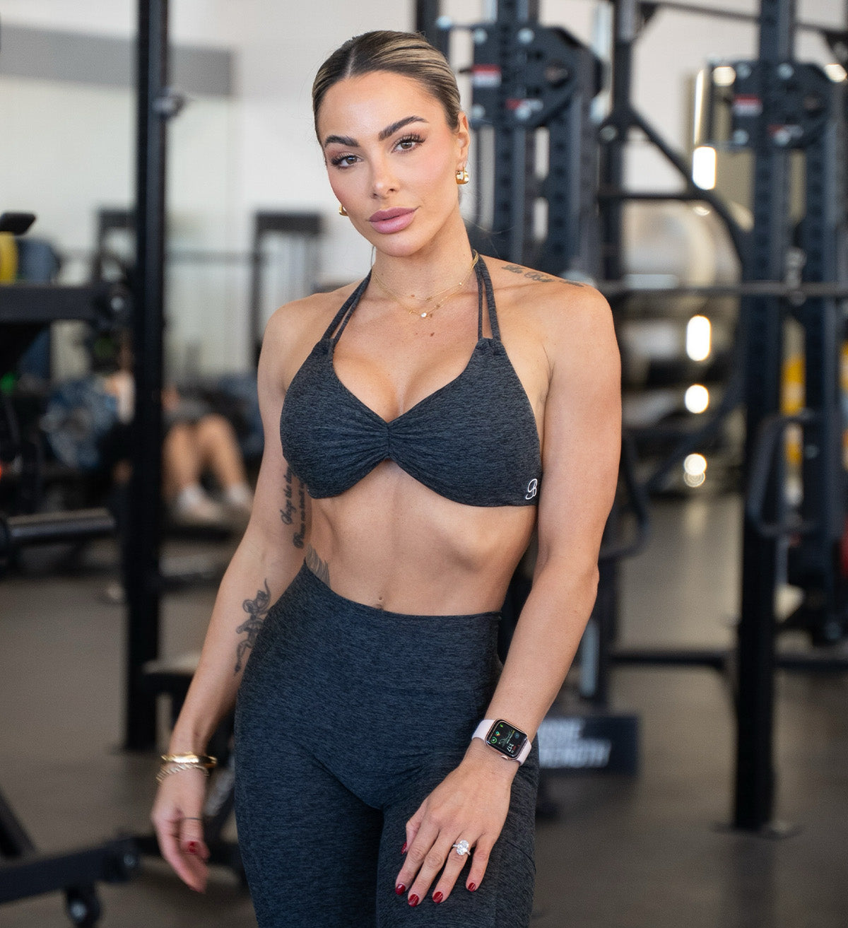 Woman in a dark sports bra and leggings standing in a gym.