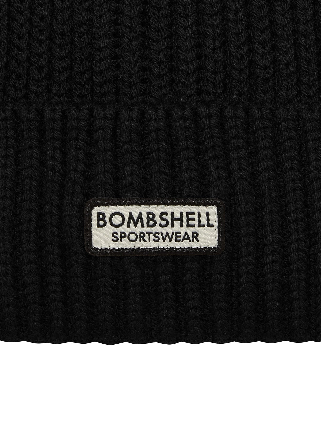 Close-up of the silver Bombshell Sportswear logo on a black B Beanie knit performance hat.
