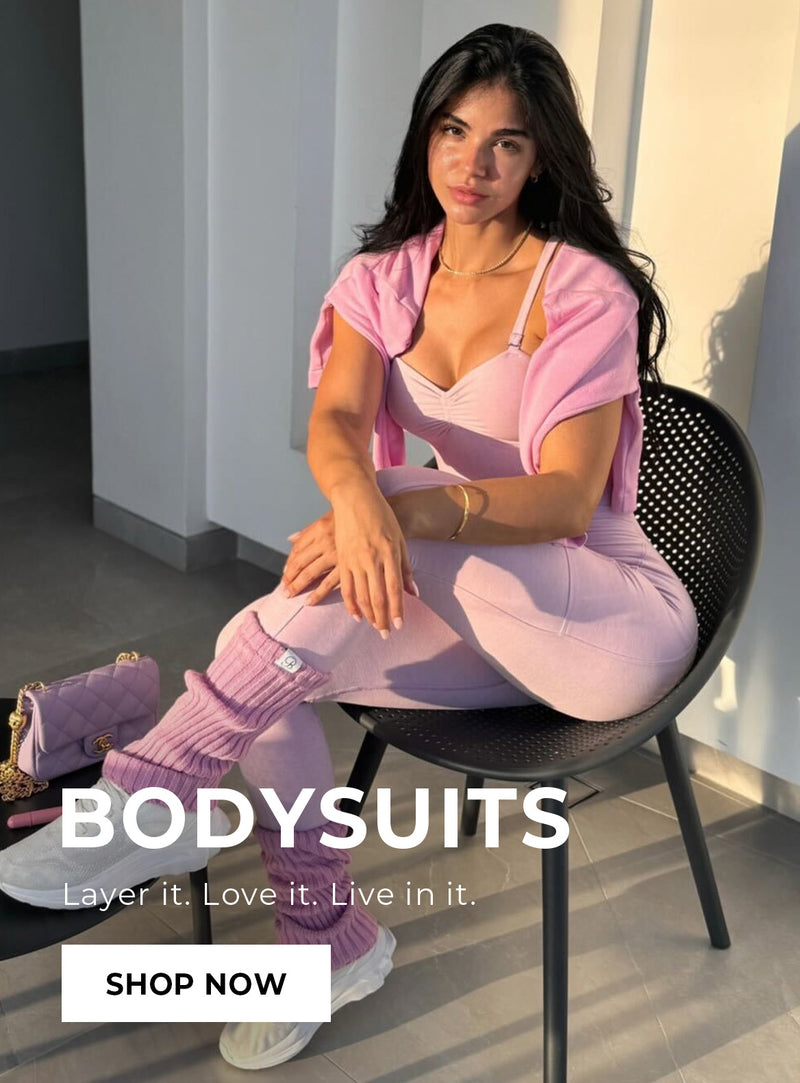 Woman in pink bodysuit sitting on a chair with promotional text for bodysuits. text reads: "BODY SUITS layer it. Love it. Live in it. SHOP NOW"