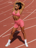 Woman stretching outdoors in Neon Tangerine Shock Lift Contour Shorts and matching sports bra.