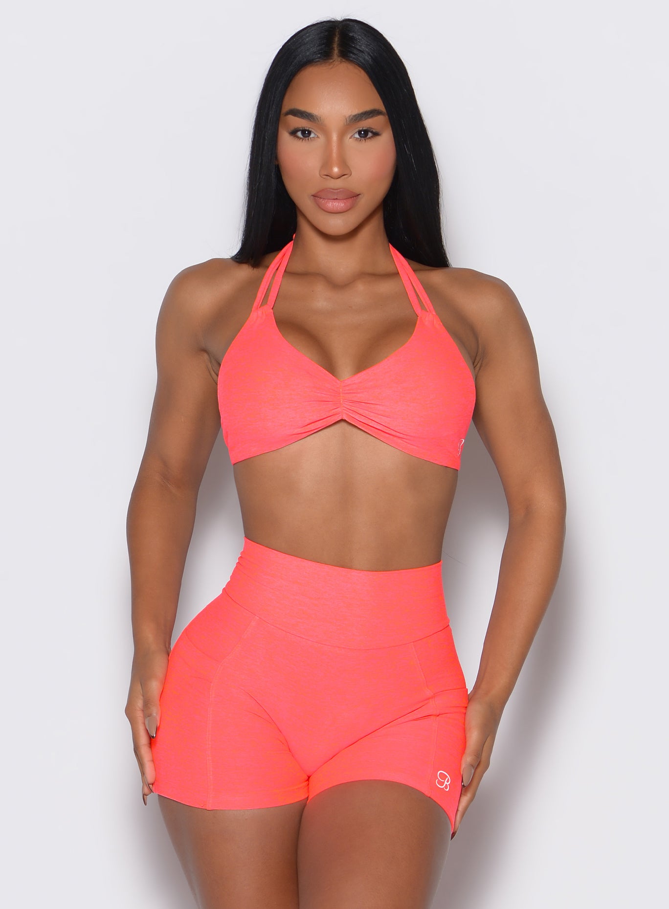 front profile view of a model wearing our butterfly sports bra in Neon Apricot Pink color along with the matching shorts 