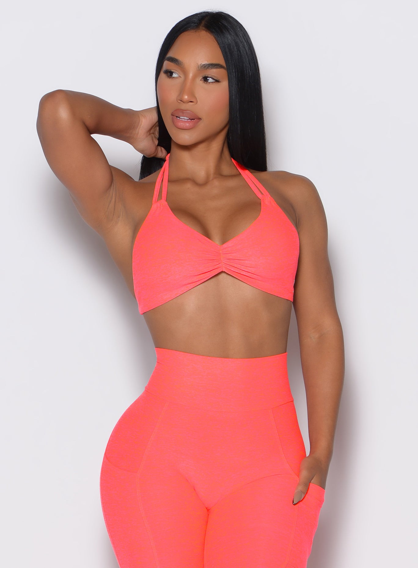 front profile view of a model wearing our butterfly sports bra in Neon Apricot Pink color along with the matching leggings