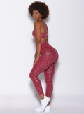 Left side profile view of a model facing to her left wearing our shine leopard leggings in Raspberry Leopard color along with a matching sports bra