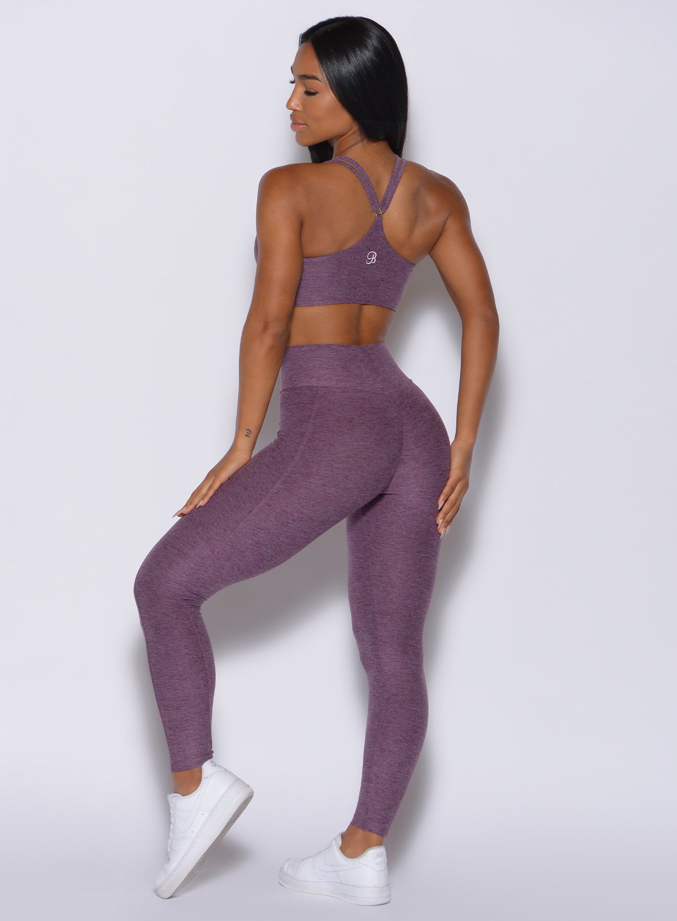 Back profile view of a model wearing our cloud leggings in regal purple color and a matching sports bra