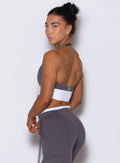 Back left side view of model looking over shoulder wearing Bombshell Sportswear Confidence bra top in Champion Grey color, featuring open back design and sculpting supportive fit