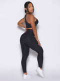 right side view of a model facing to her right wearing our Contour Leggings and the matching Cross Over Halter Bra in Heathered Black color
