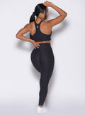 back profile of a model wearing the Contour Leggings and the matching Cross Over Halter Bra in Heathered Black color
