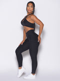 left side view of a model facing to her left wearing our Contour Leggings and the matching Cross Over Halter Bra in Heathered Black color
