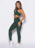 Left side view of model wearing the Contour Leggings and the matching Cross Over Halter Bra in Pine color
