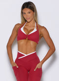 front profile view of a model with both hands inside the side pockets of the leggings wearing the Contrast Voltage Sports Bra in maroon color