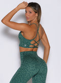 back left side profile view of a model looking over her shoulder wearing the Cross Fit Bra in Emerald Green Cheetah color