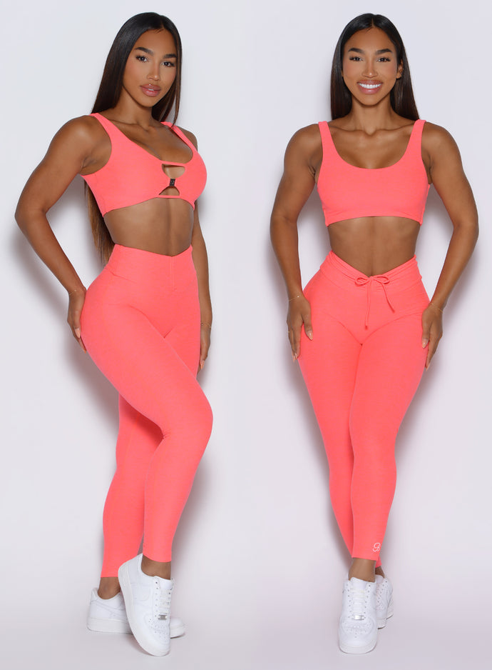 front profile view of a model showcasing the straight and V cut waistband side by side wearing the Curvemax leggings in neon apricot pink color 