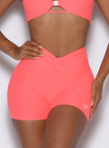 zoomed in front view of a model with one hand on her waist wearing the Curvemax shorts in neon apricot pink color