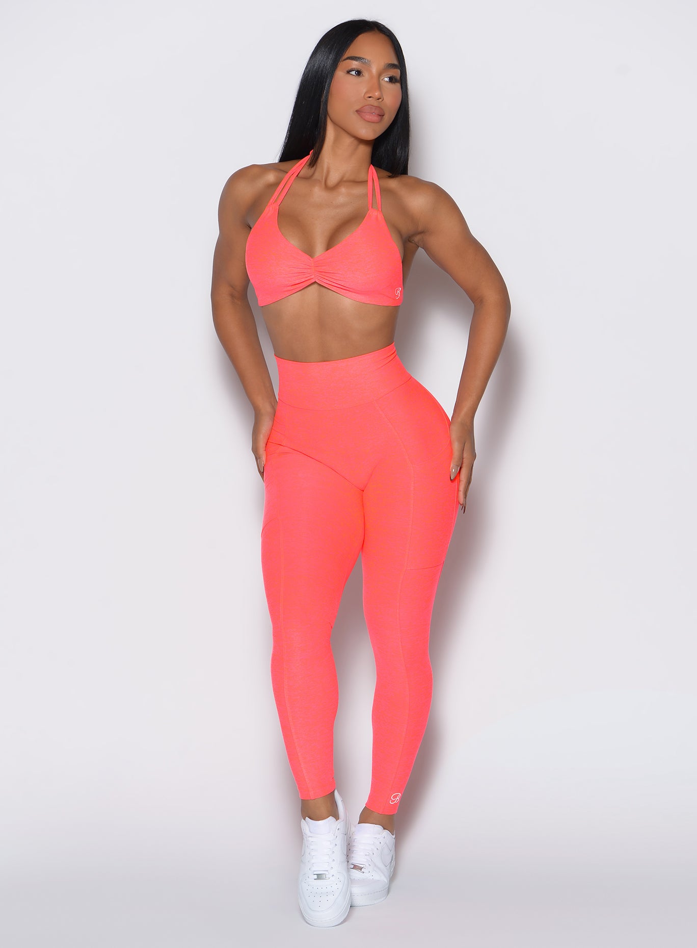 front profile picture of a model wearing our curves leggings in Neon Apricot Pink color along with the matching sports bra