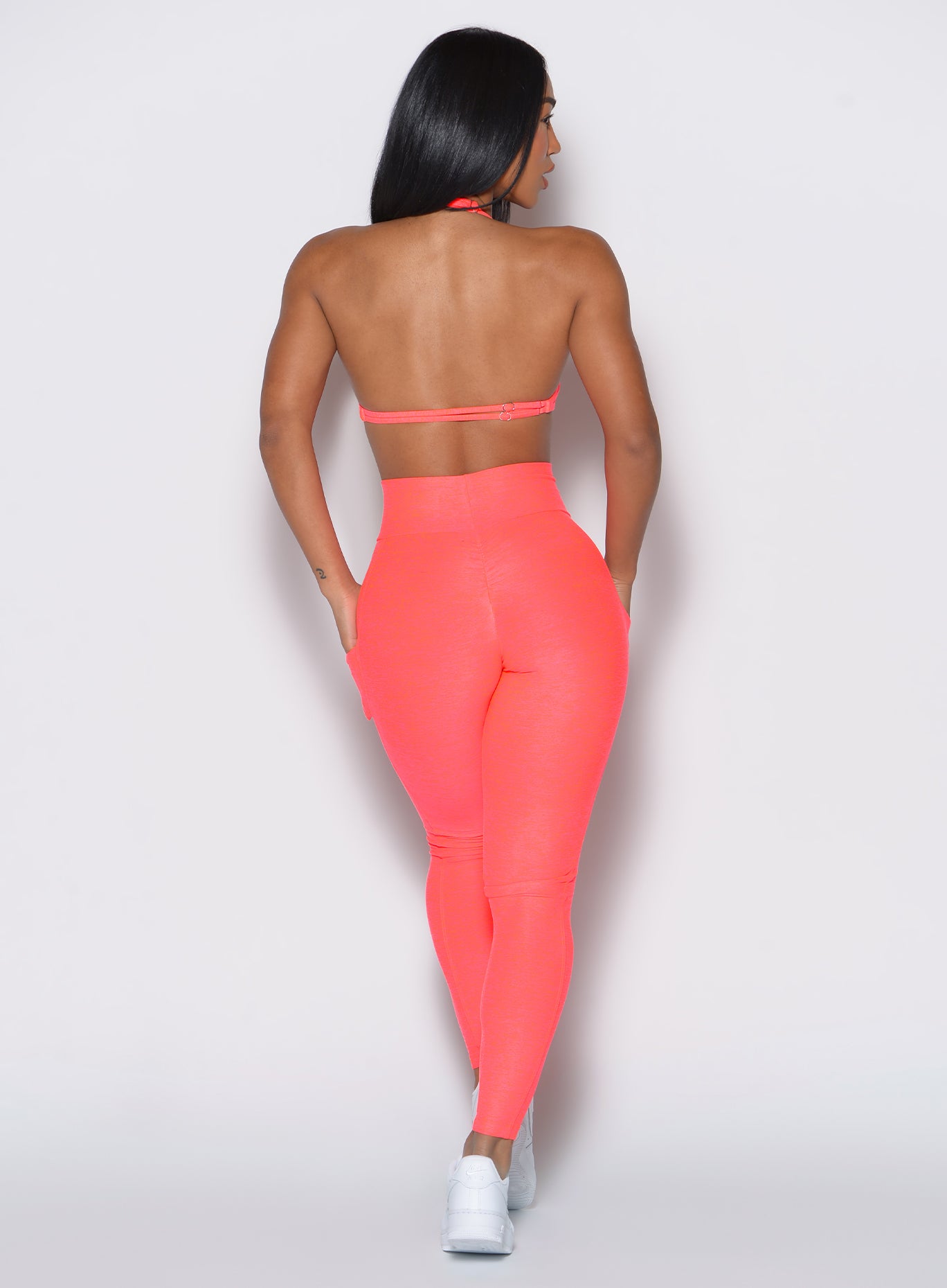 back profile picture of a model facing to her right wearing our curves leggings in Neon Apricot Pink color along with the matching sports bra