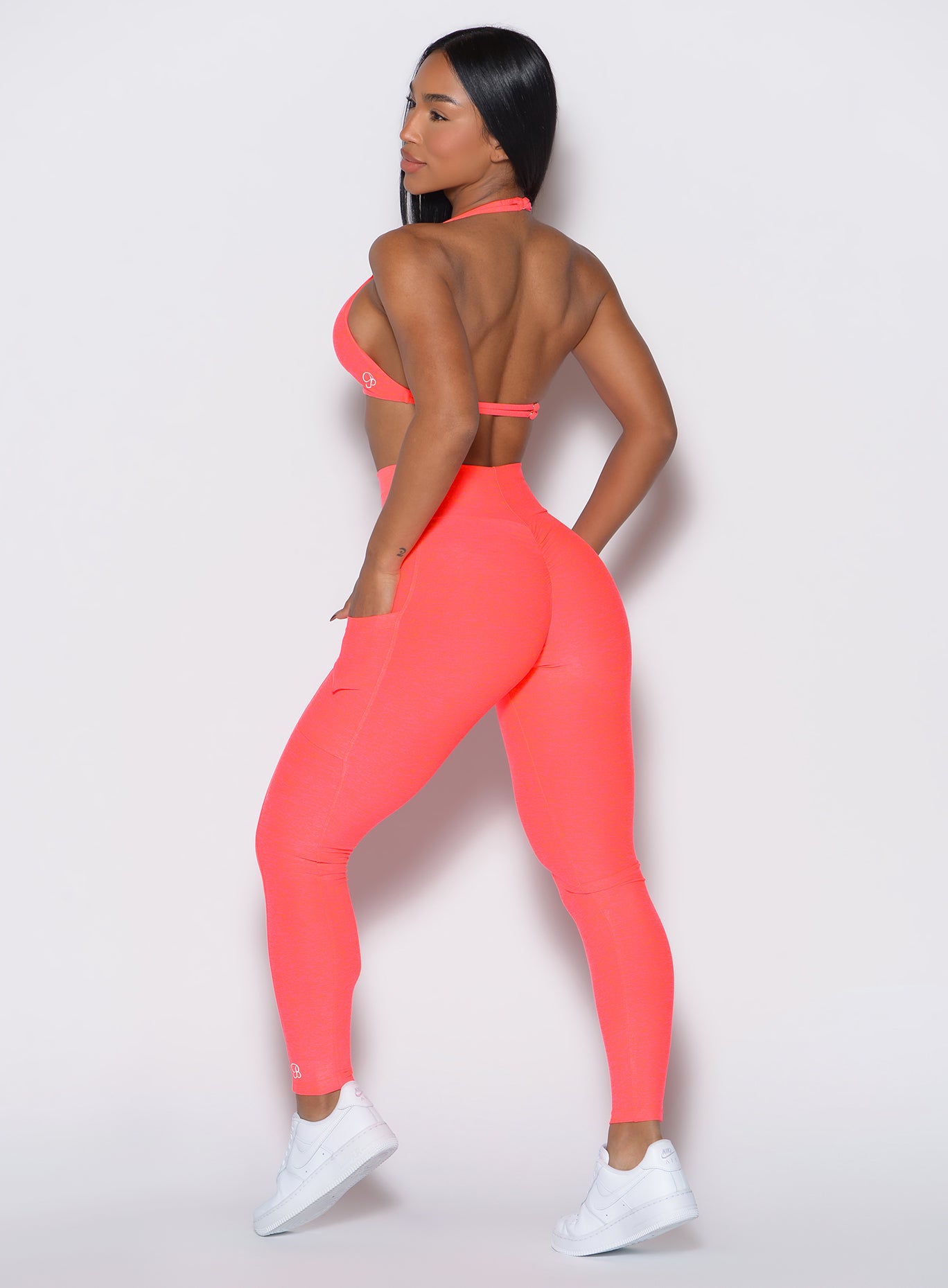 back profile view of a model wearing our curves leggings in Neon Apricot Pink color along with the matching sports bra