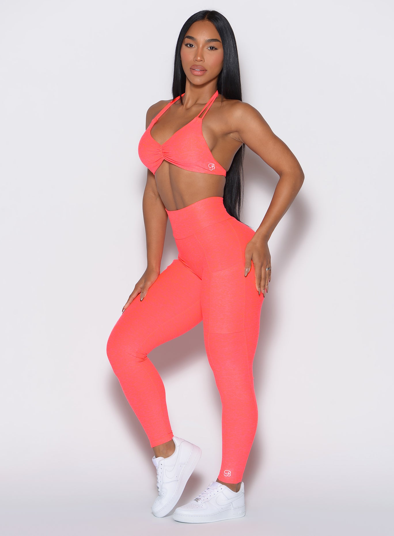 front profile view of a model angled slightly to her right wearing our curves leggings in Neon Apricot Pink color along with the matching sports bra