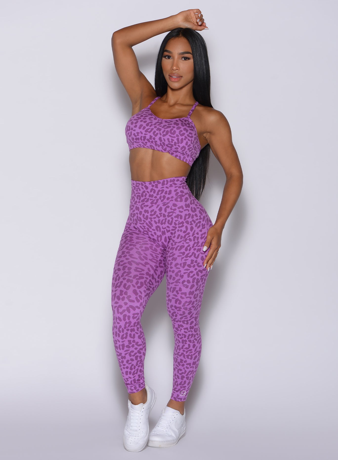 Front profile view of a model facing forward wearing our curves leggings in purple cheetah color and a matching sports bra