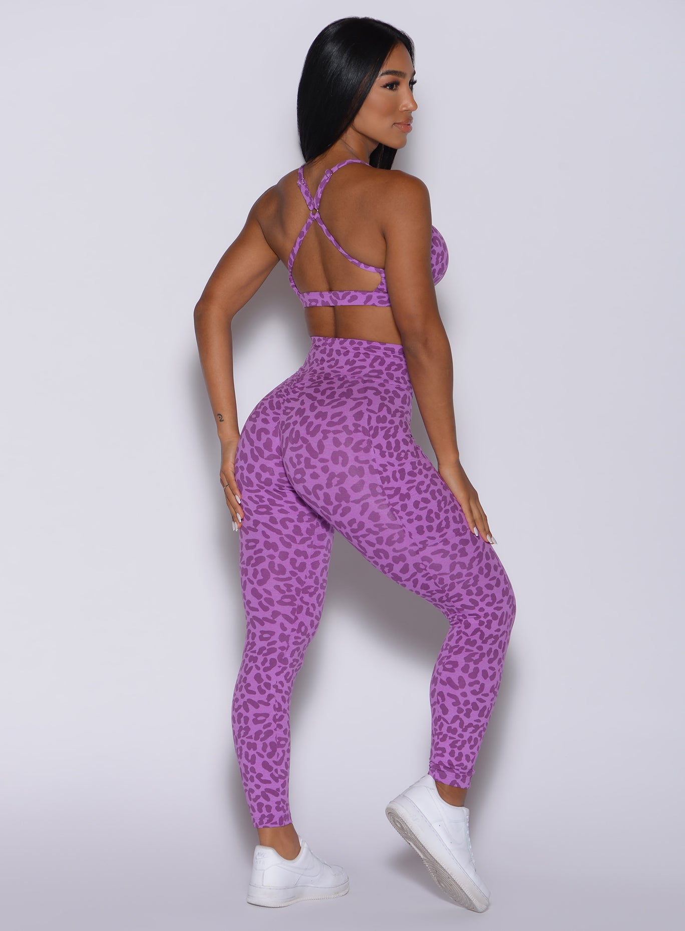Back profile view of a model in our curves leggings in purple cheetah color and a matching sports bra