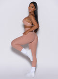 left side profile view of a model wearing our Curves leggings in Nude Sand color, paired with the matching sports bra.