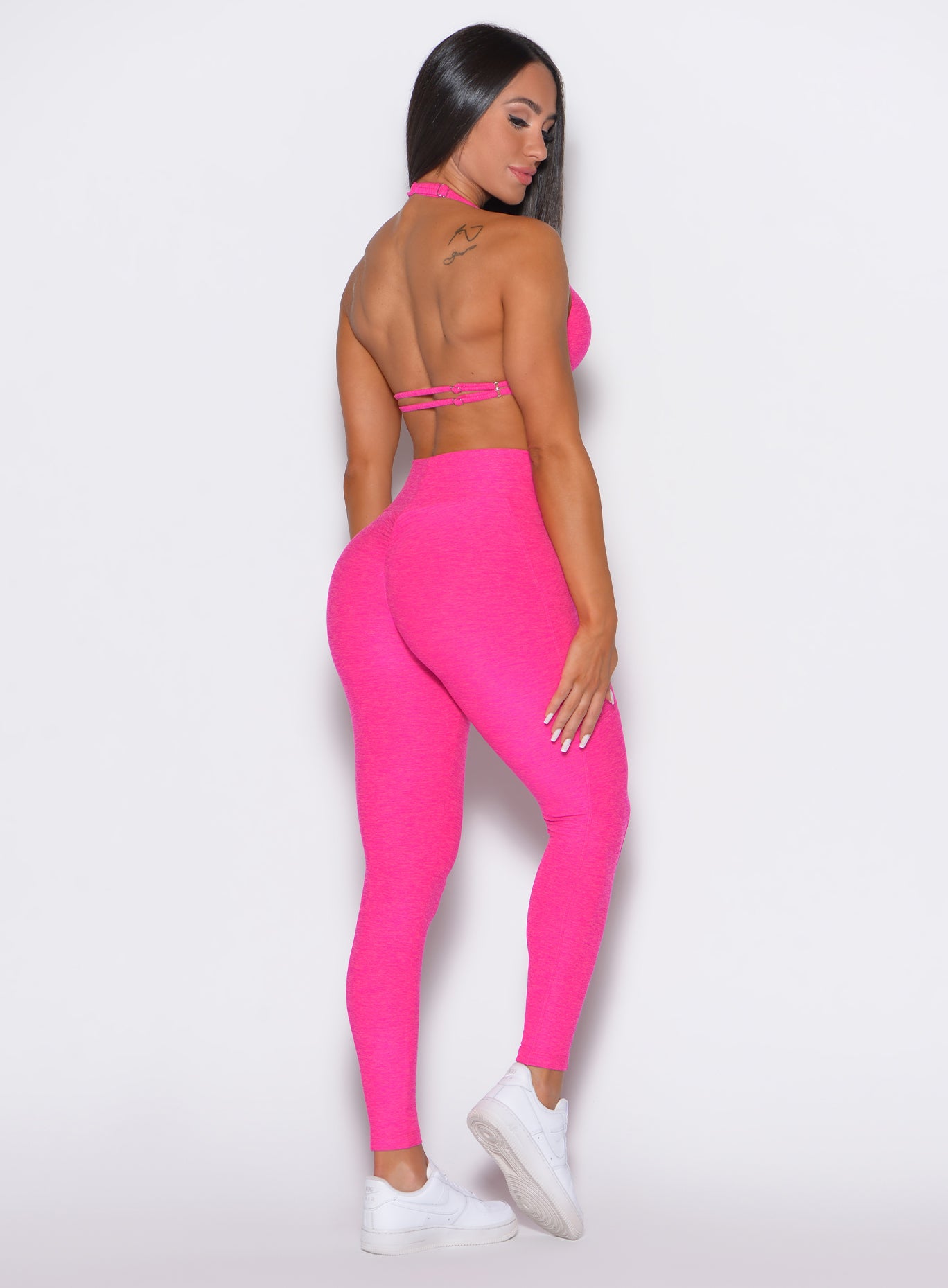back  profile view of a model facing to her right wearing our curves leggings in Neon Pink Berry color along with the matching bra