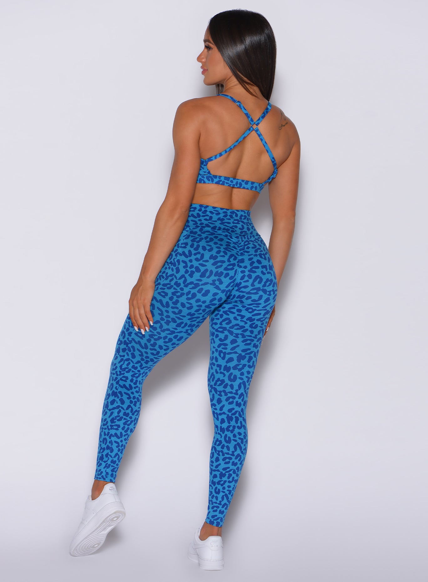 Back profile view of a model facing to her left wearing our curves leggings in blue cheetah color and a matching bra