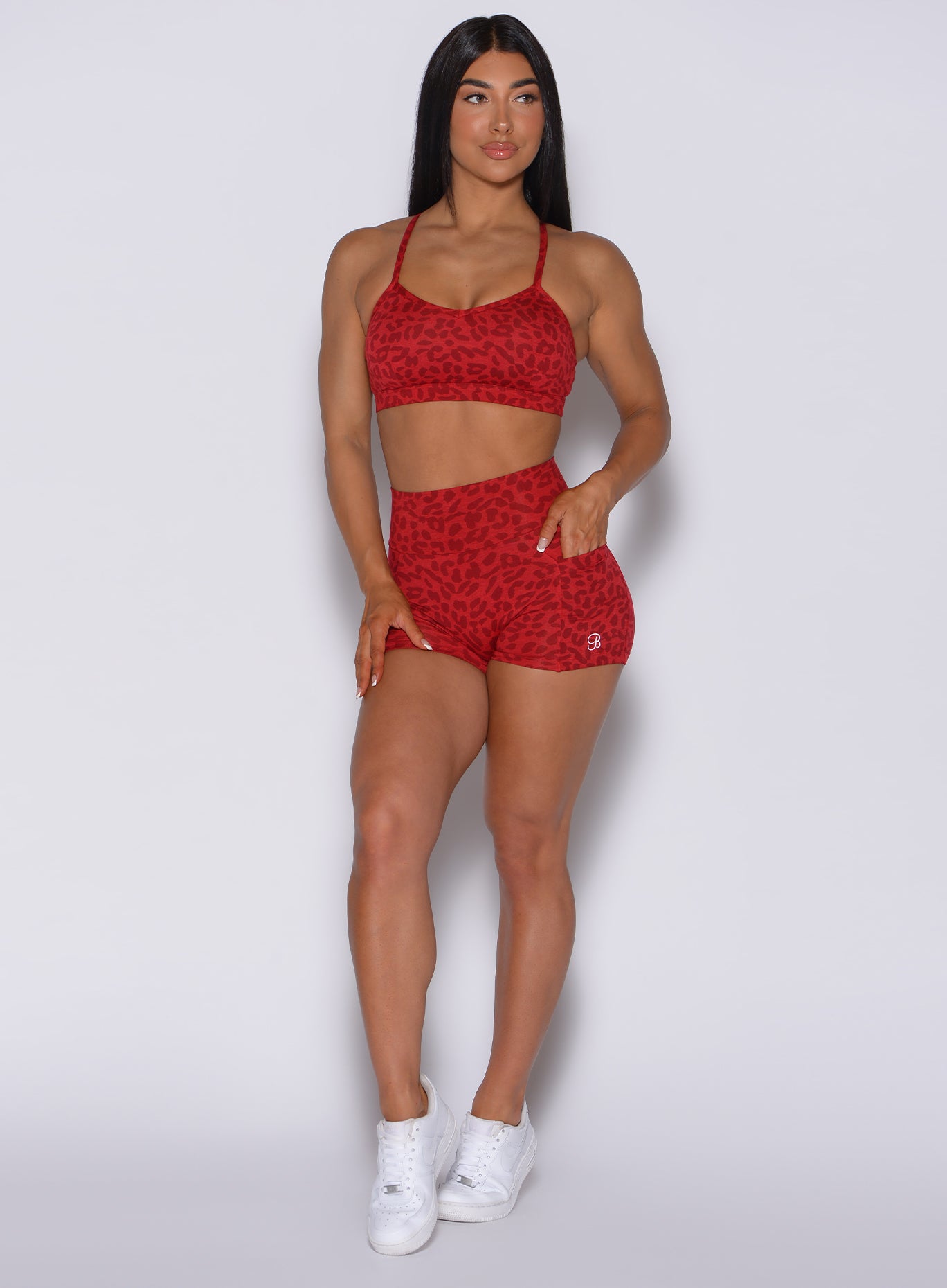 Front  profile view of a model with her left hand in pocket wearing our curves shorts in red cheetah color along with a matching bra