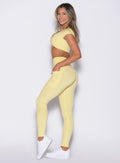 left side profile view of a model wearing the Define Leggings in Soft Yellow color paired with the matching top