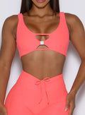 close up front view of a model wearing the Dualmode Bra in neon apricot pink color with the B logo hardware in front