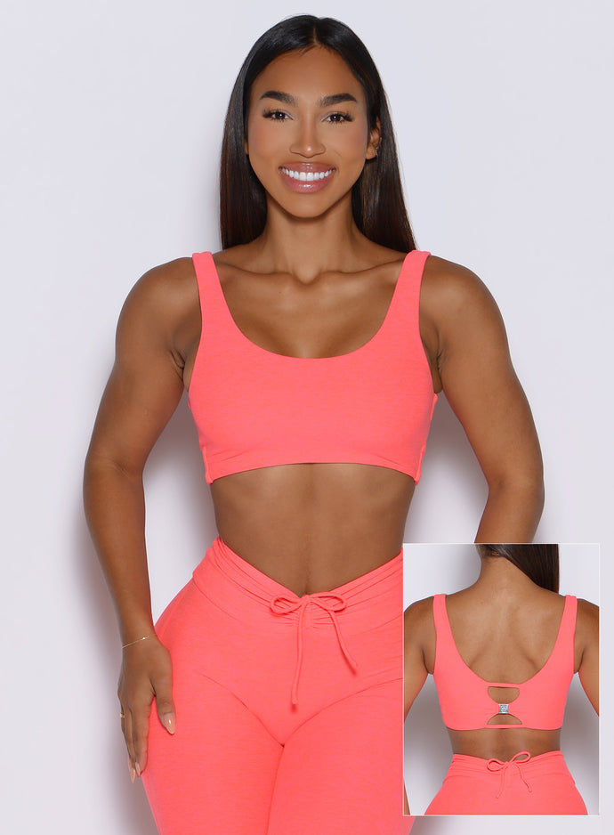 front profile view of a model highlighting the two way style of the Dualmode Bra in neon apricot pink color with the plain side in front and the B log on the back side