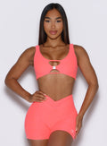 model captured from the front with one hand on her waist wearing the Dualmode Bra in Neon apricot pink color