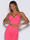 front view of a model adjusting the waistband of the leggings wearing the Electric Era Top in neon flame color