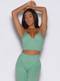 front view of a model with both hands resting on top of her head wearing the Electric Era Top in sage color