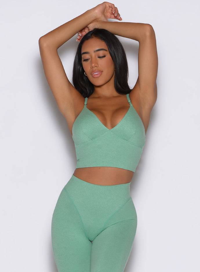 front view of a model with both hands resting on top of her head wearing the Electric Era Top in sage color