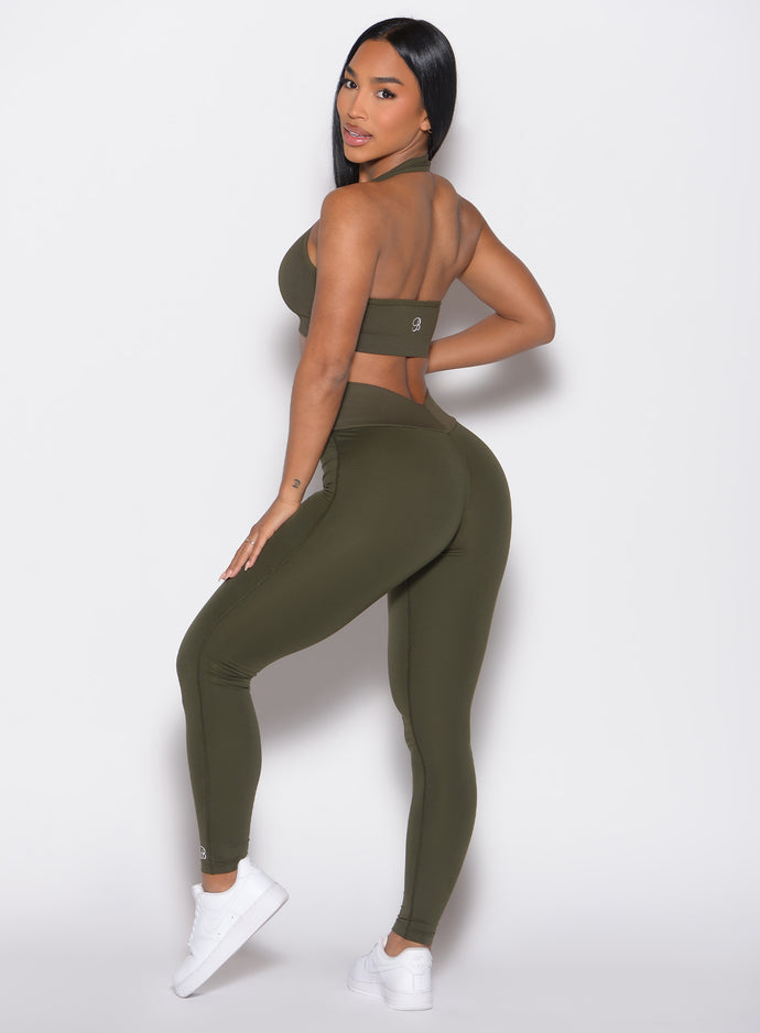 back left side profile view of a model looking over her shoulder wearing the Figure Butt Lift Leggings in forest night color