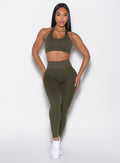 front profile view of a model with both hands resting on her thighs wearing the Figure Butt Lift Leggings in forest night color