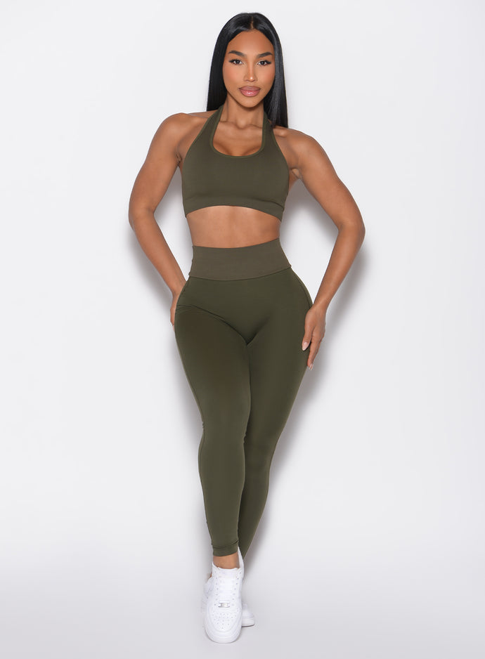 front profile view of a model with both hands resting on her thighs wearing the Figure Butt Lift Leggings in forest night color