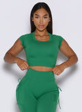 front profile view of a model adjusting the waistband of the leggings wearing the FitBoost Tee in Field green color