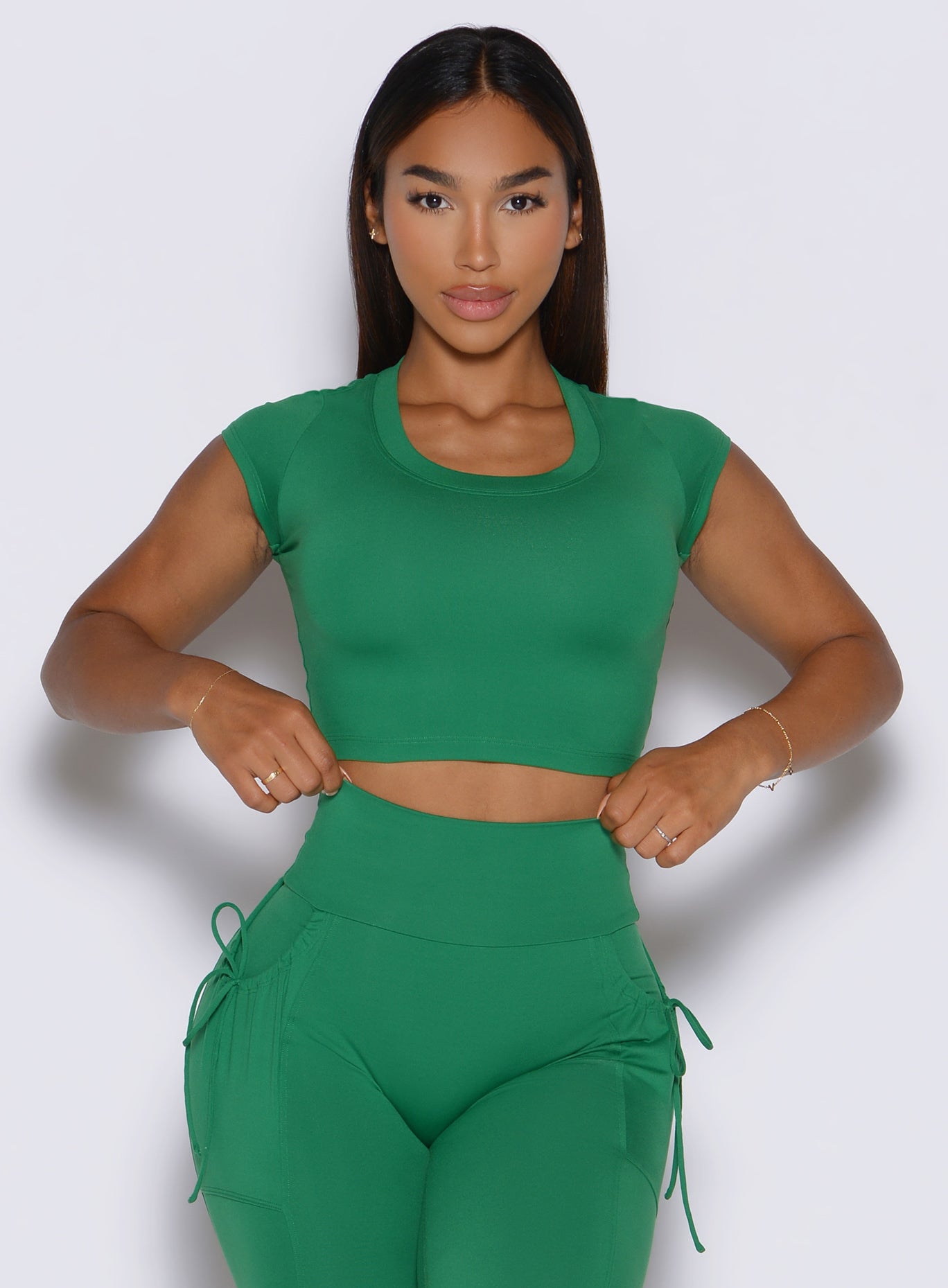 front profile view of a model adjusting the waistband of the leggings wearing the FitBoost Tee in Field green color