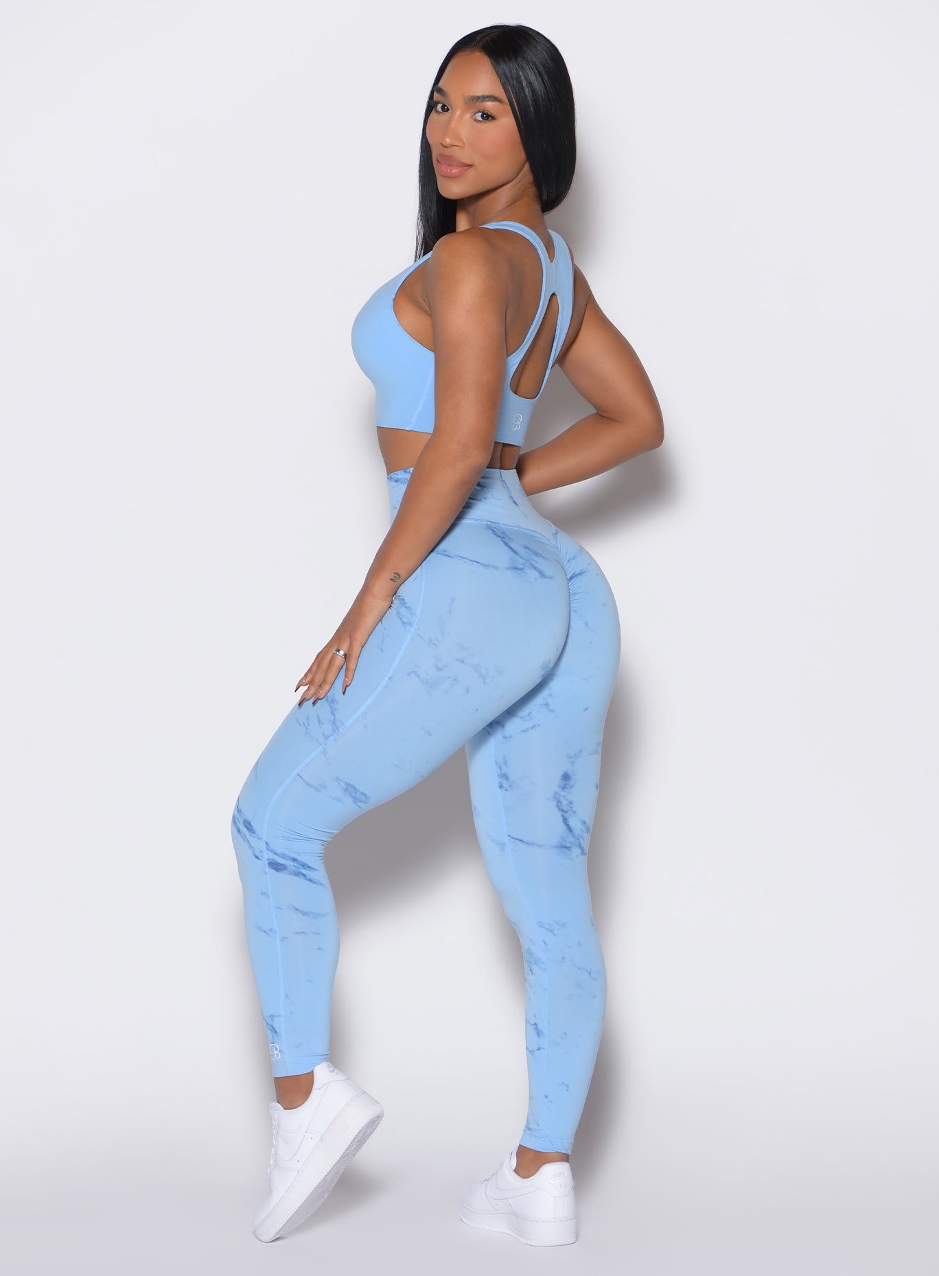 left side profile view of a model wearing our fit marble leggings in Blue Jay color along with a matching bra 