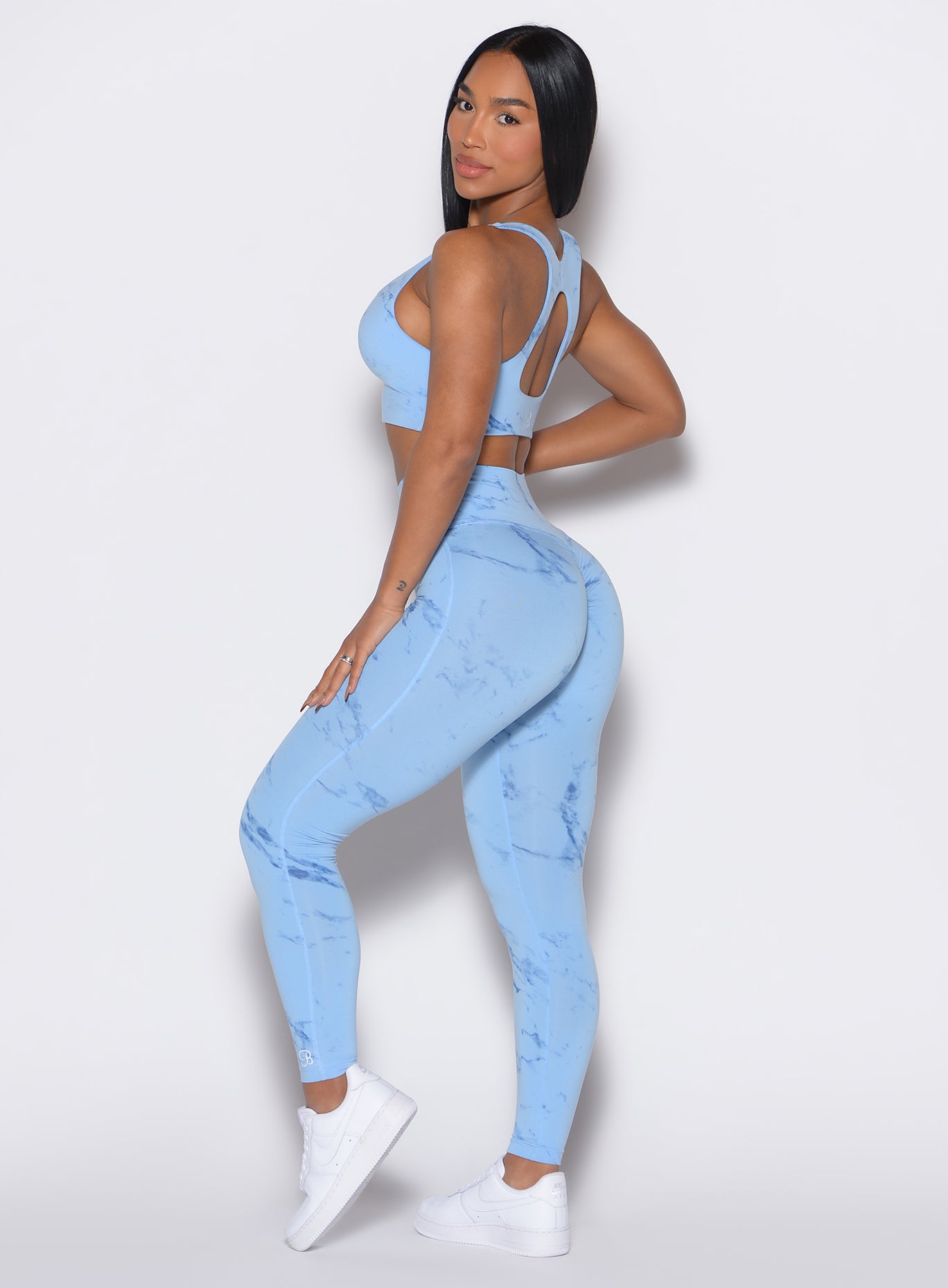 left side  profile view of a model facing to her left wearing our fit marble leggings in Blue Jay color along with a matching bra