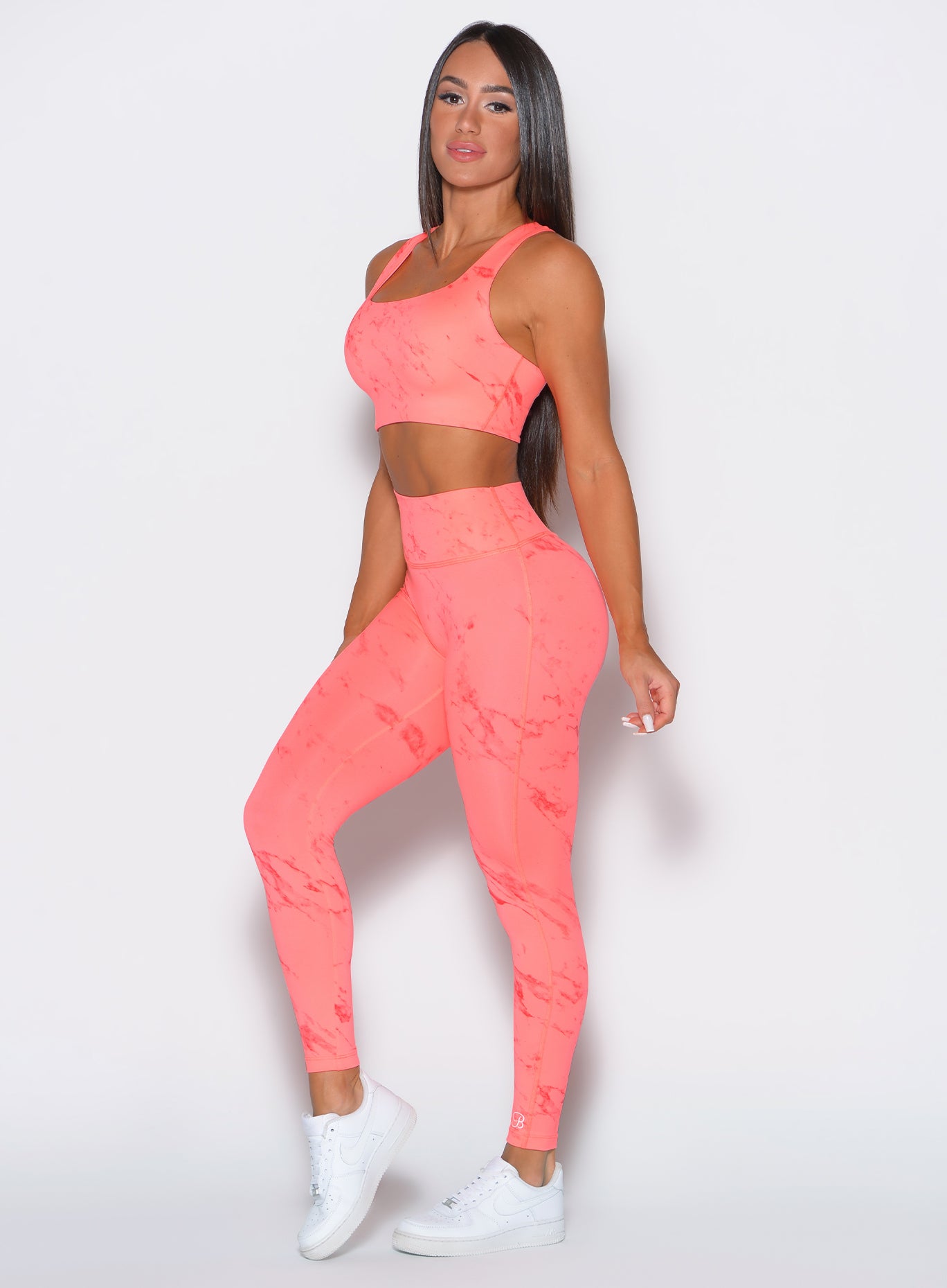 left side profile view of a model facing to the camera wearing our fit marble leggings in Coral reef color along with a matching bra