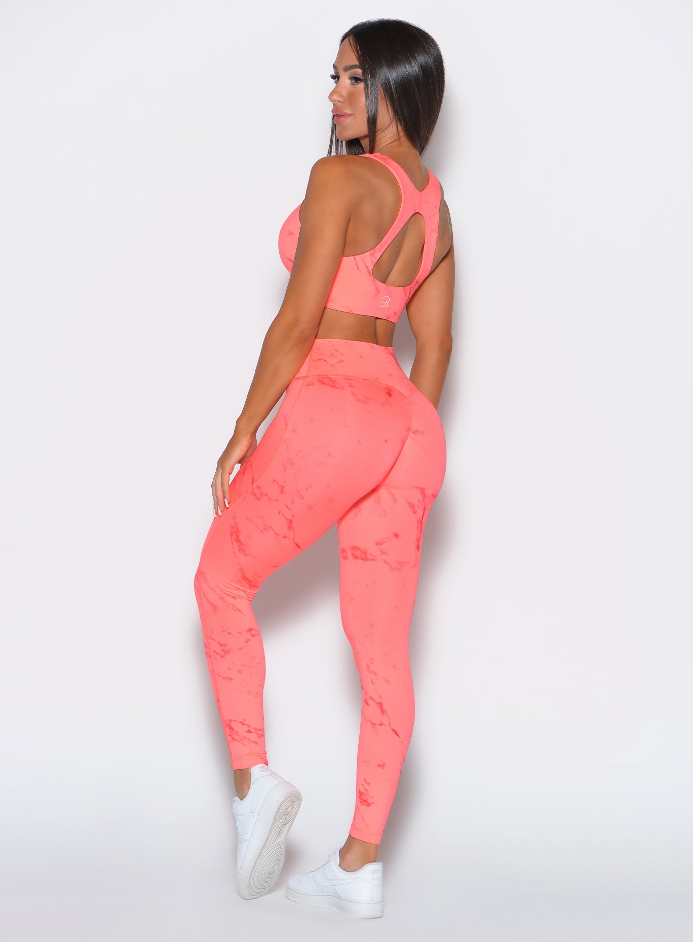 left side profile view of a model facing to her left wearing our fit marble leggings in Coral reef color along with a matching bra