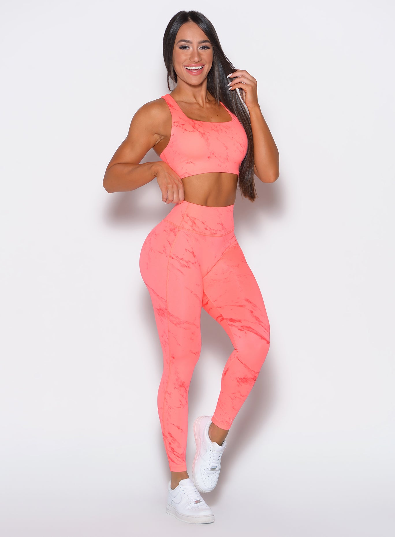 front profile view of a model facing forward wearing our fit marble leggings in Coral reef color along with a matching bra