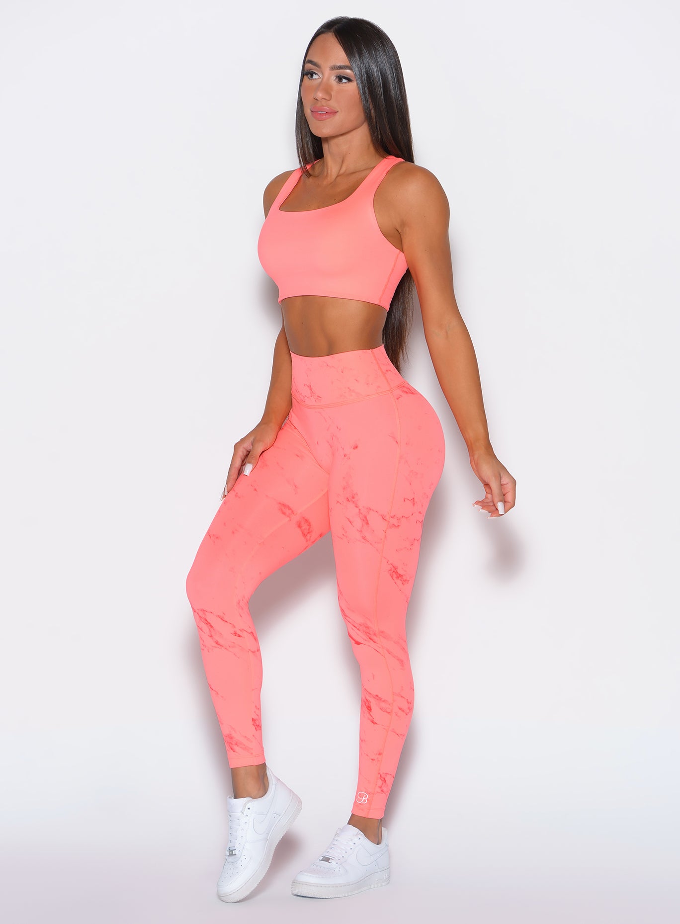 left side profile view of a model angled slightly to her left wearing our fit marble leggings in Coral reef color along with a matching bra