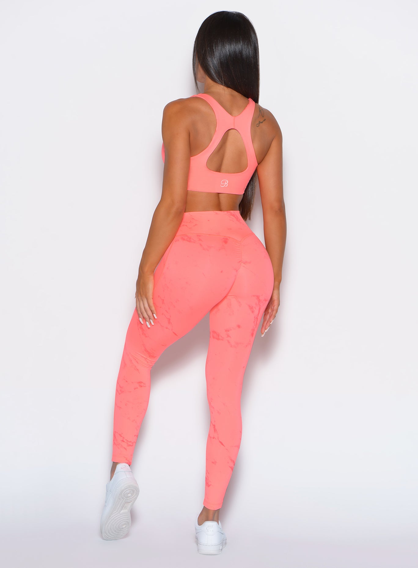 back profile view of a model wearing our fit marble leggings in Coral reef color along with a matching bra
