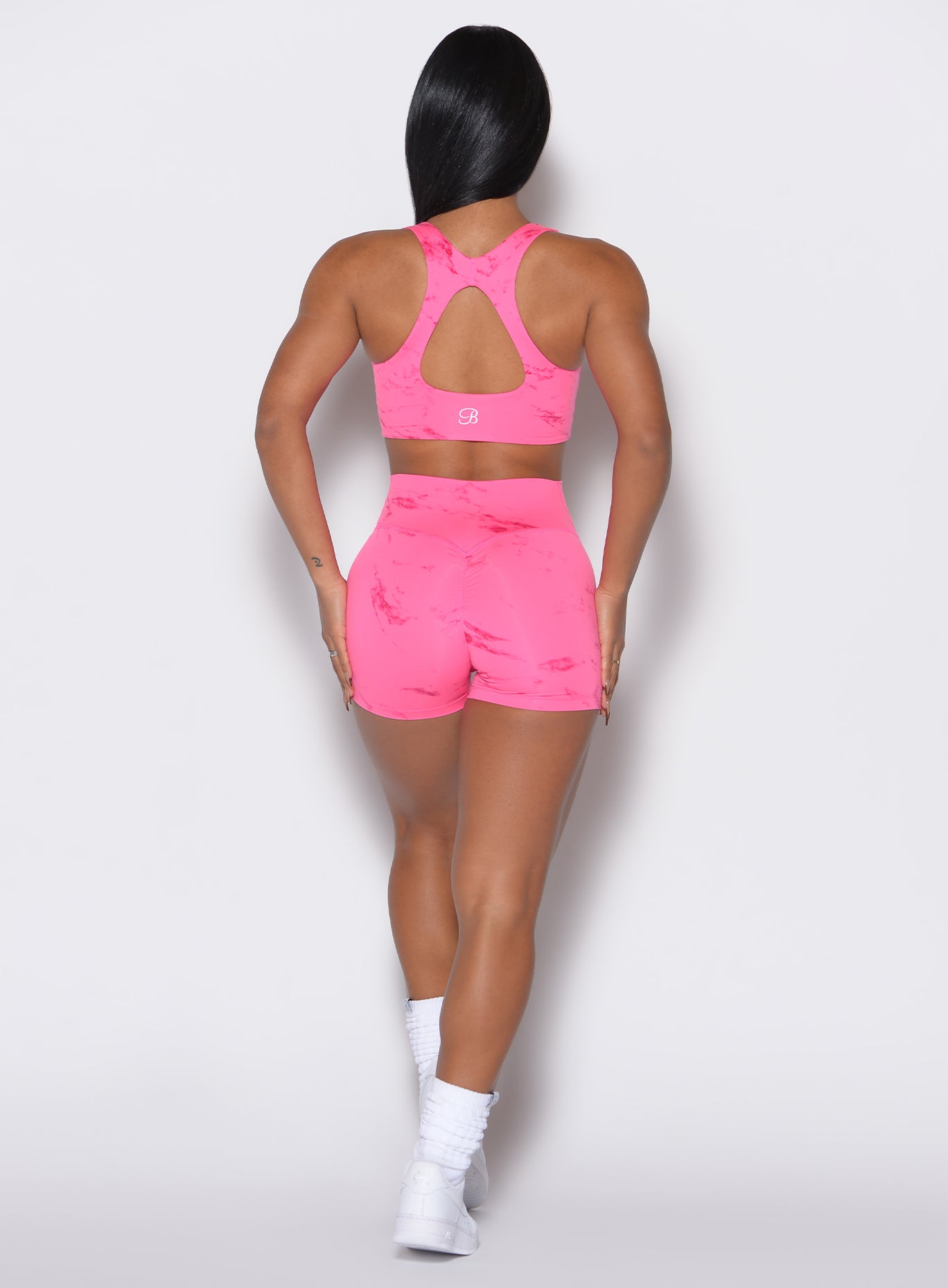 back profile view of a model wearing our fit marble shorts in Cotton Candy Skies color along with a matching sports bra