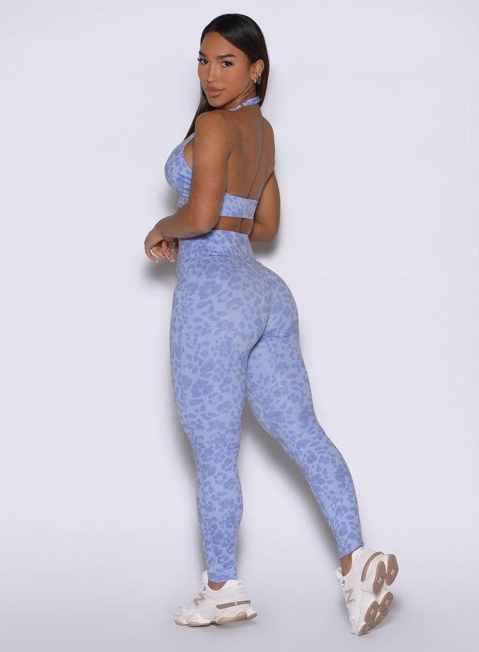 Back left side angle view of the model posing looking over her shoulder with her hands in front wearing our Flexfit leggings in Leopard Baby Lavender paired with the matching top.