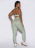 Right-back view of the model wearing our Flexfit leggings in Leopard Cool Matcha, posing with left hand on hip and right hand on thigh.