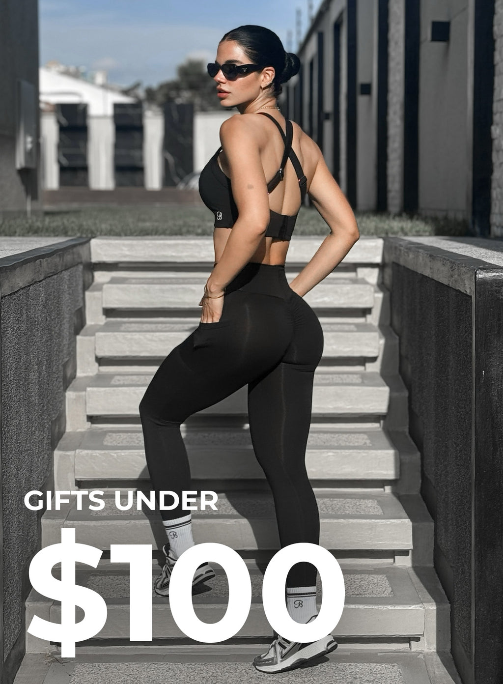 Front left view of model wearing black active set. bottom left corner says GIFTS UNDER $100 in white text